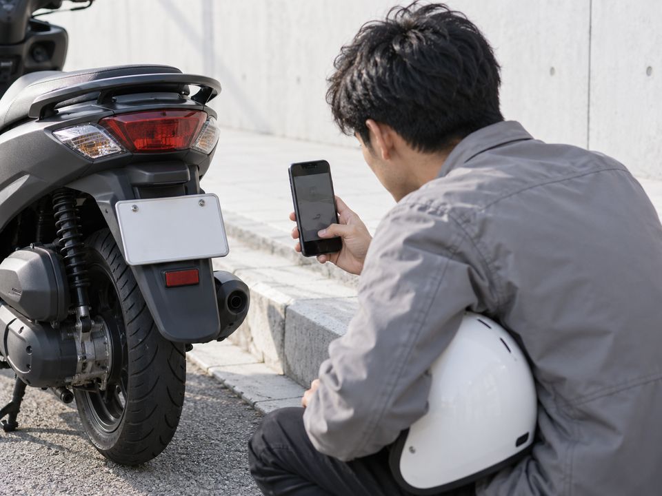 A delivery rider points the phone's back camera at the scooter's number plate.